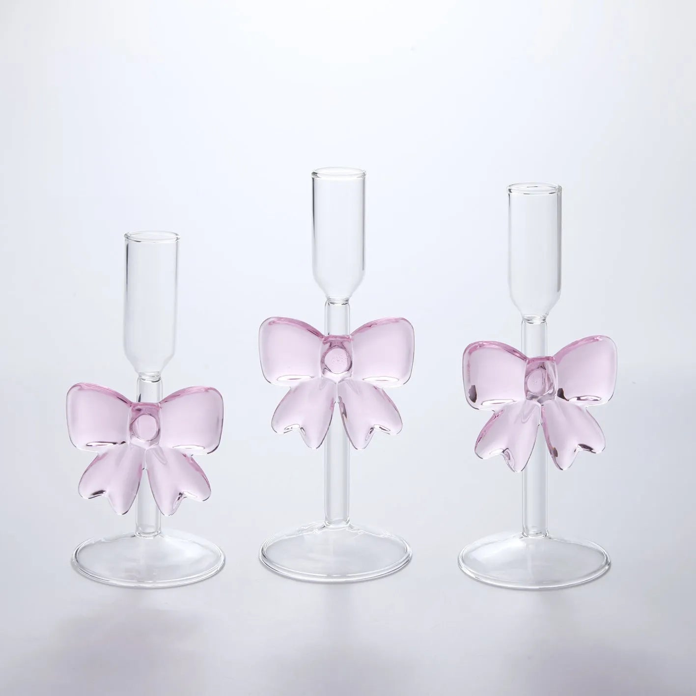 Set of three clear borosilicate glass candlesticks with large bow decorations on a table
