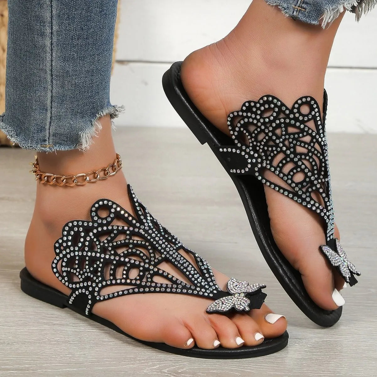 Women's black slip-on sandals with rhinestone detail, hollow-out design, and flat rubber sole.