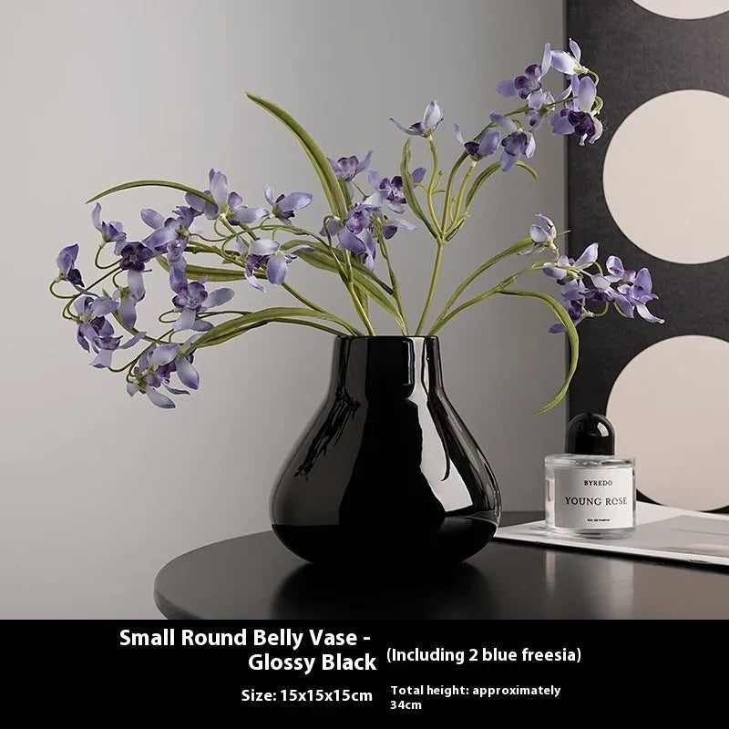 Black ceramic round belly vase with white artificial orchids on wooden table