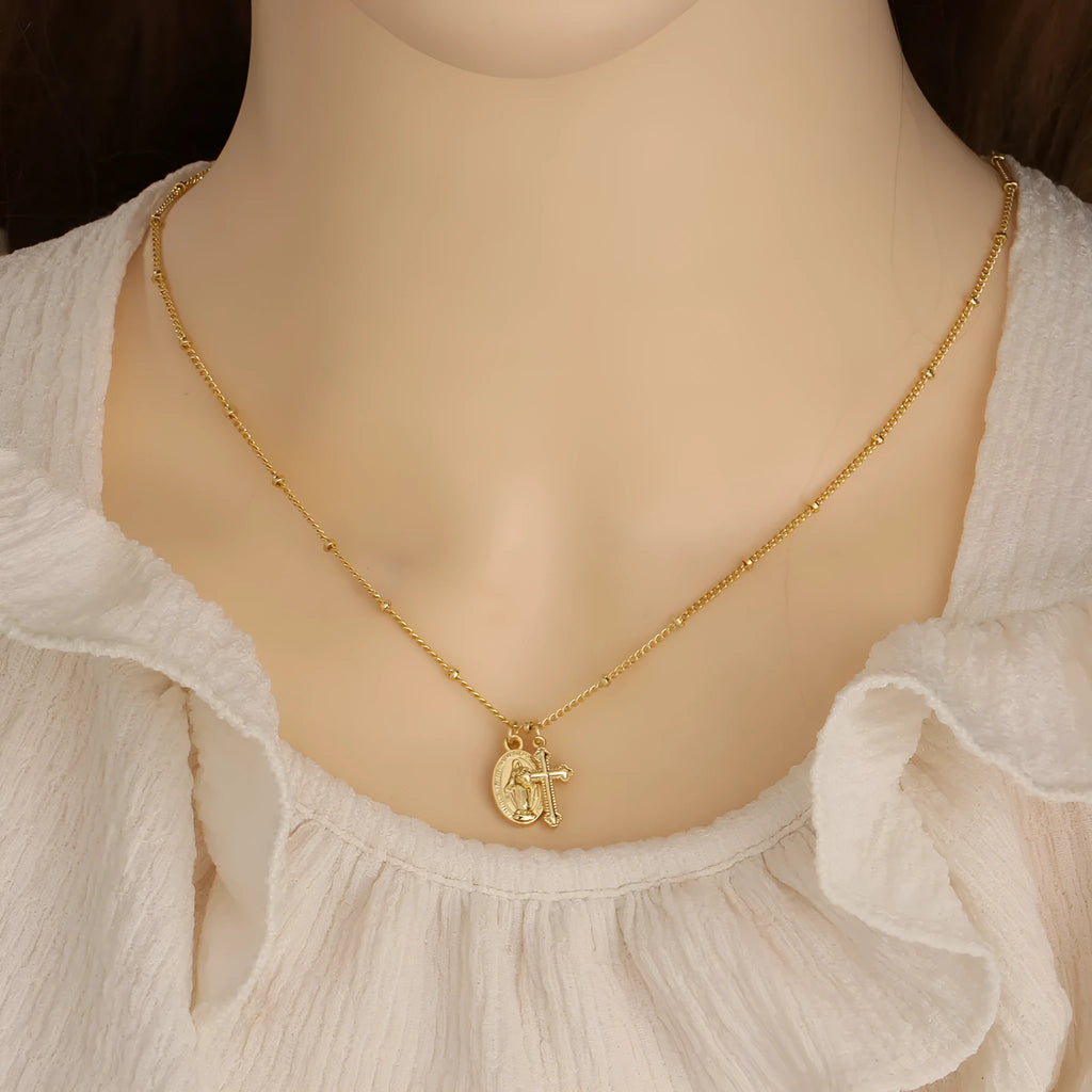 Gold-coloured geometric Virgin Mary and cross pendant necklace on a chain.