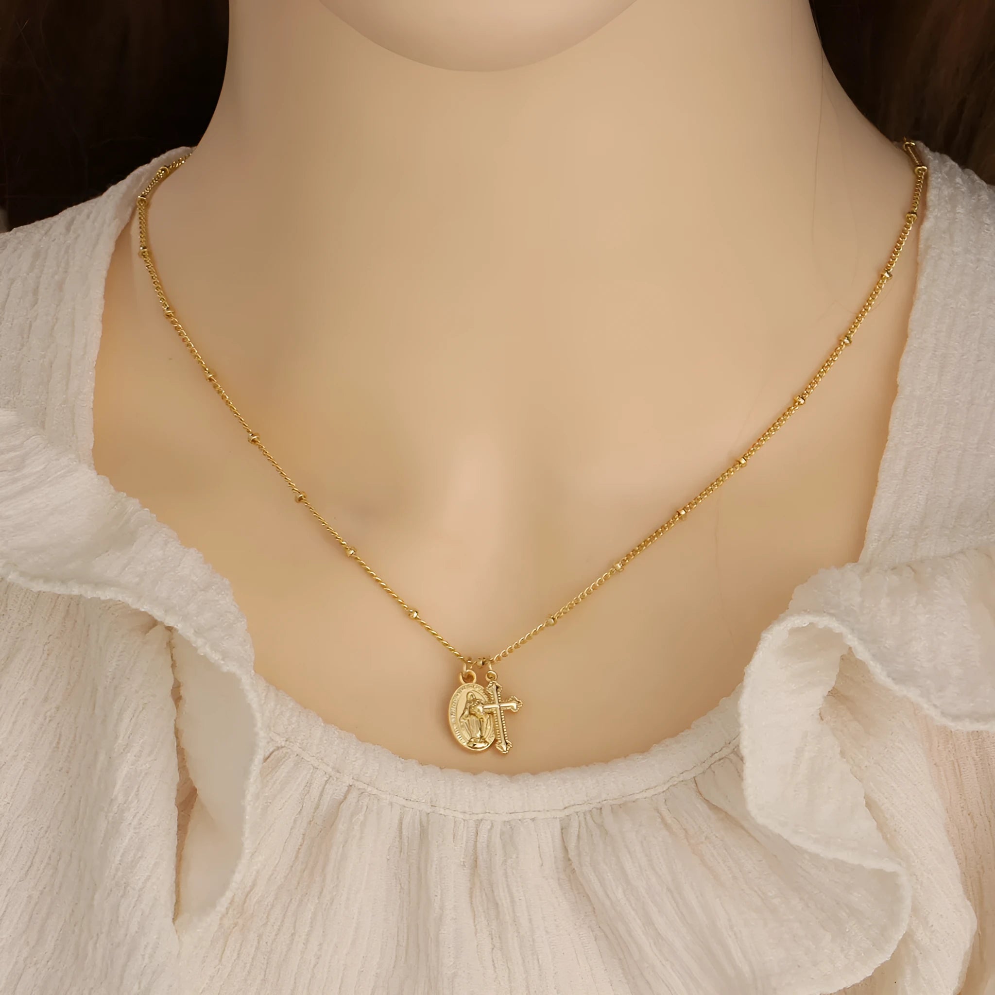Gold-coloured geometric Virgin Mary and cross pendant necklace on a chain.