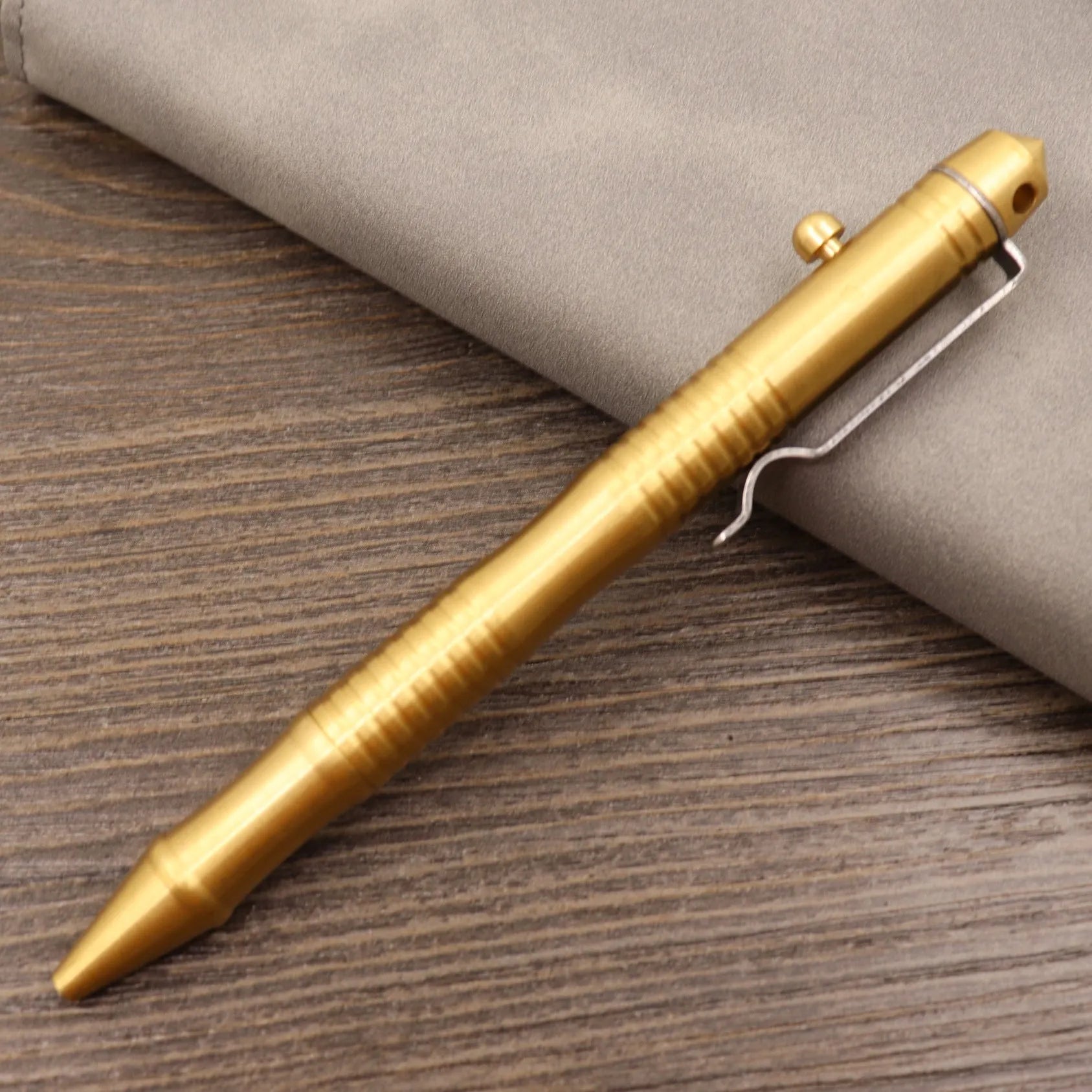 Close-up of a solid brass bolt action tactical pen with a press mechanism on a dark surface.