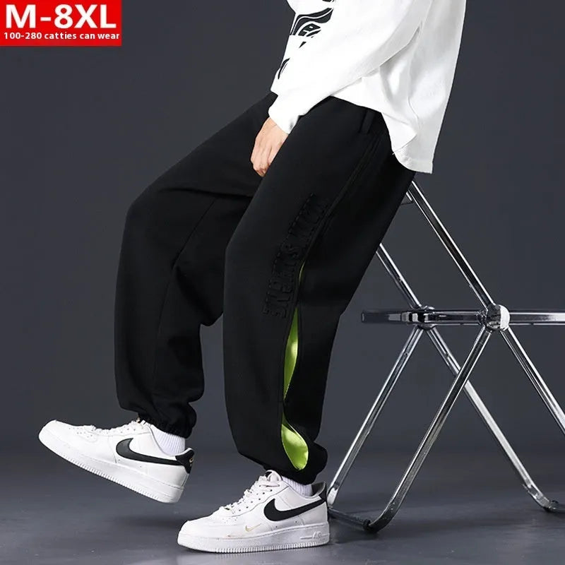 Men's loose black cotton trousers with white collage stitching print and banded ankle cuffs laid flat.