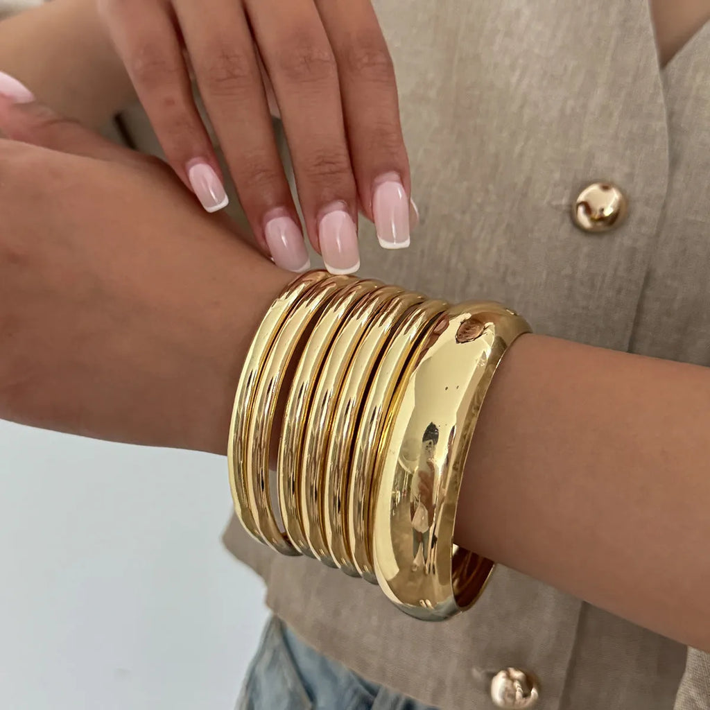 Exaggerated wide round glossy metal bracelet in gold tone on plain background