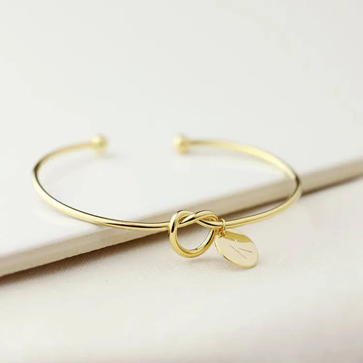 Personalised initial heart knot bracelet in gold finish with custom letter on a white background