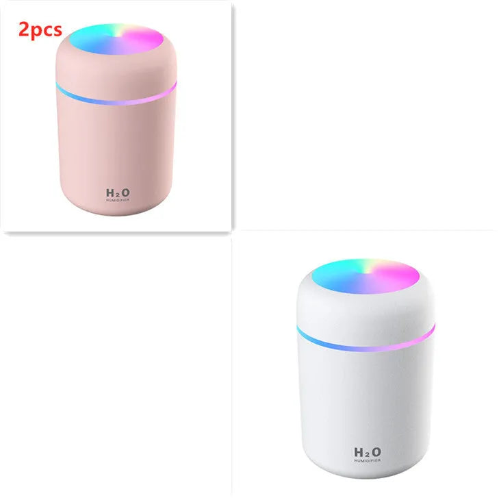 Pink USB desktop humidifier with LED lights and water tank on a wooden desk.