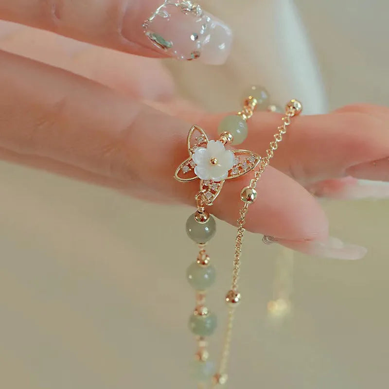 Yellow gold electroplated copper bracelet with a bells of Ireland butterfly, shell flowers, and Hetian jade accents.