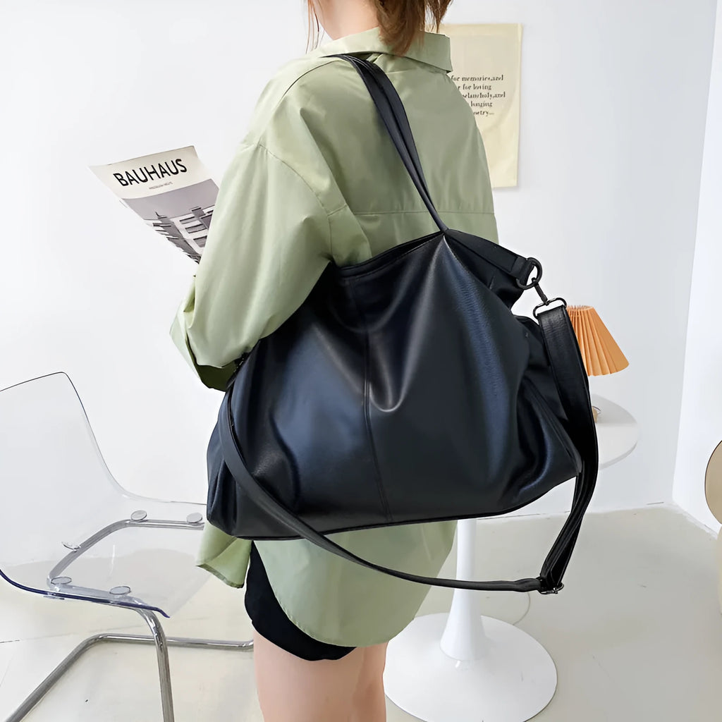 Large soft surface black messenger bag with soft handle and long shoulder strap on a table