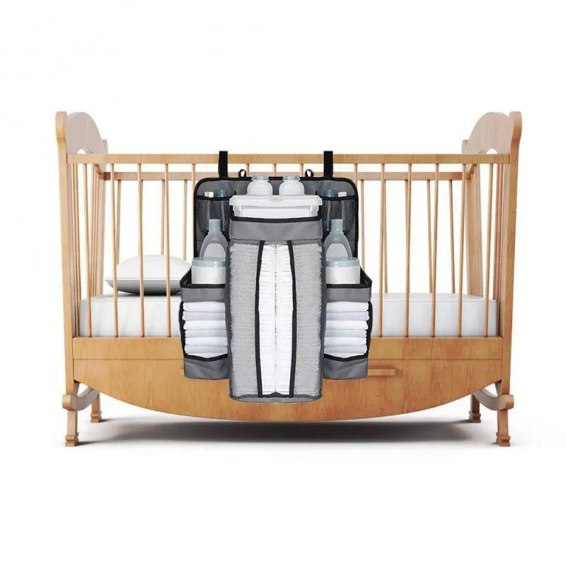 Gray baby diaper organizer hanging on a crib rail with compartments for nappies and wipes
