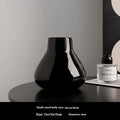 Black ceramic round belly vase with white artificial orchids on wooden table