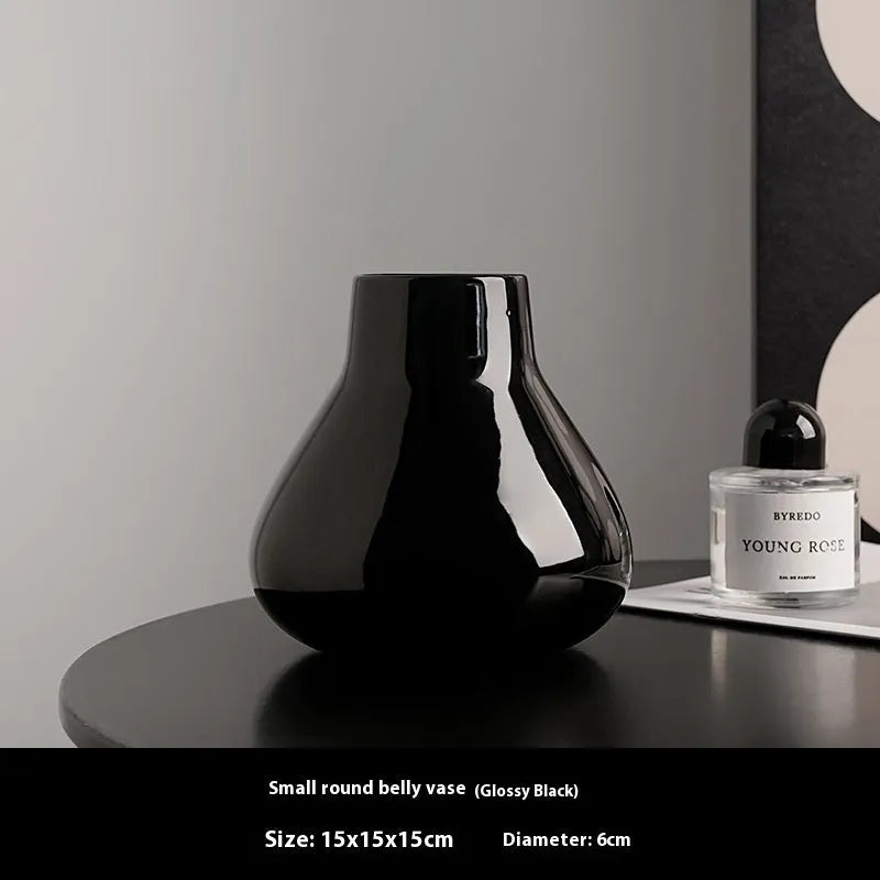 Black ceramic round belly vase with white artificial orchids on wooden table