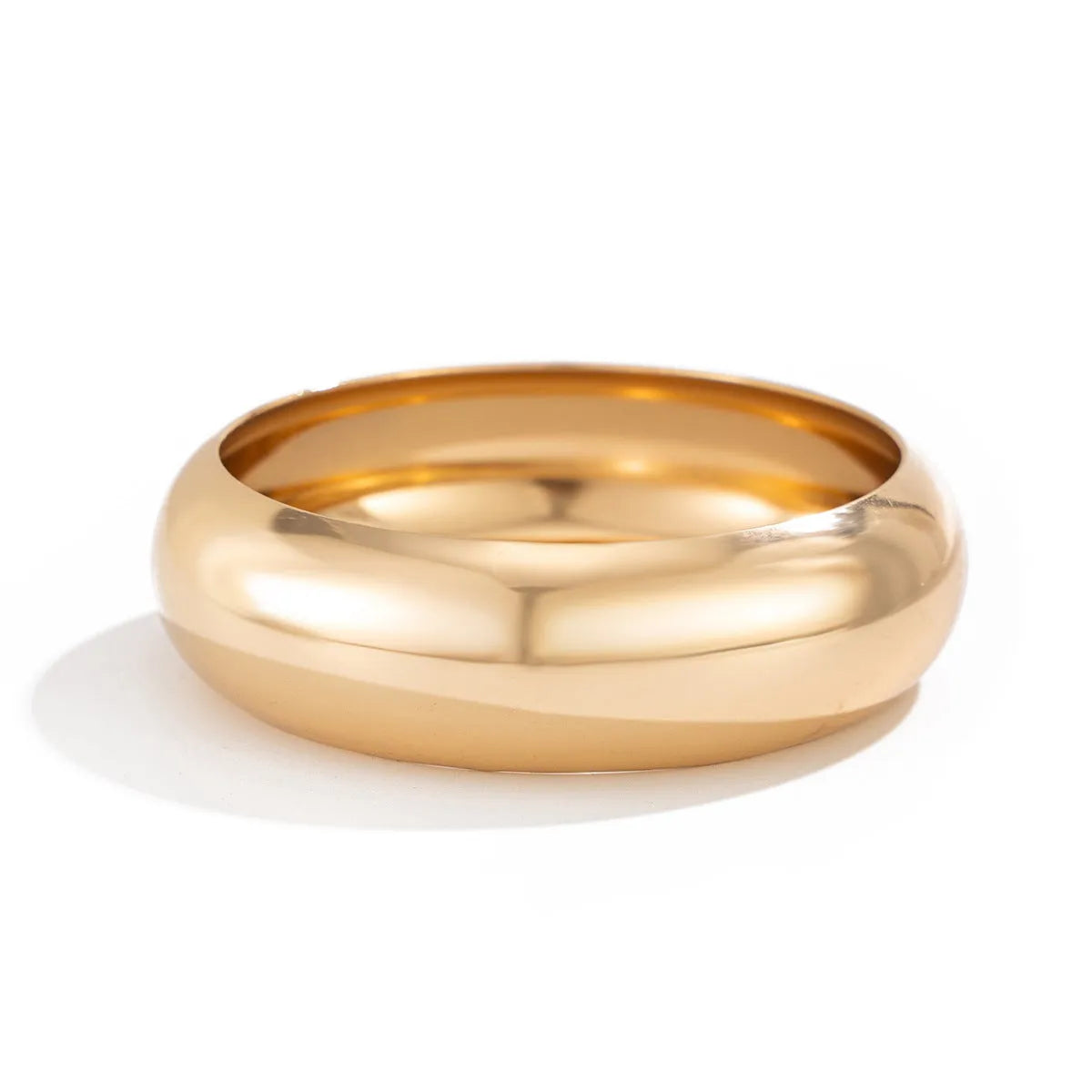 Exaggerated wide round glossy metal bracelet in gold tone on plain background
