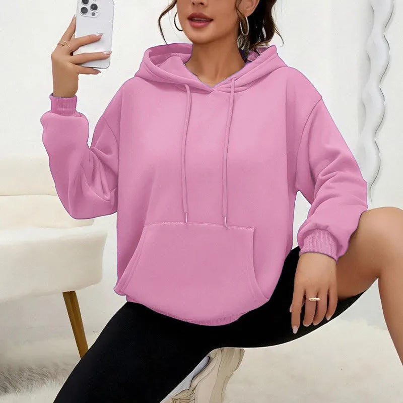 Woman wearing a loose-fitting black hooded sweatshirt with a front kangaroo pocket.