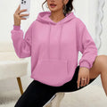 Woman wearing a loose-fitting black hooded sweatshirt with a front kangaroo pocket.