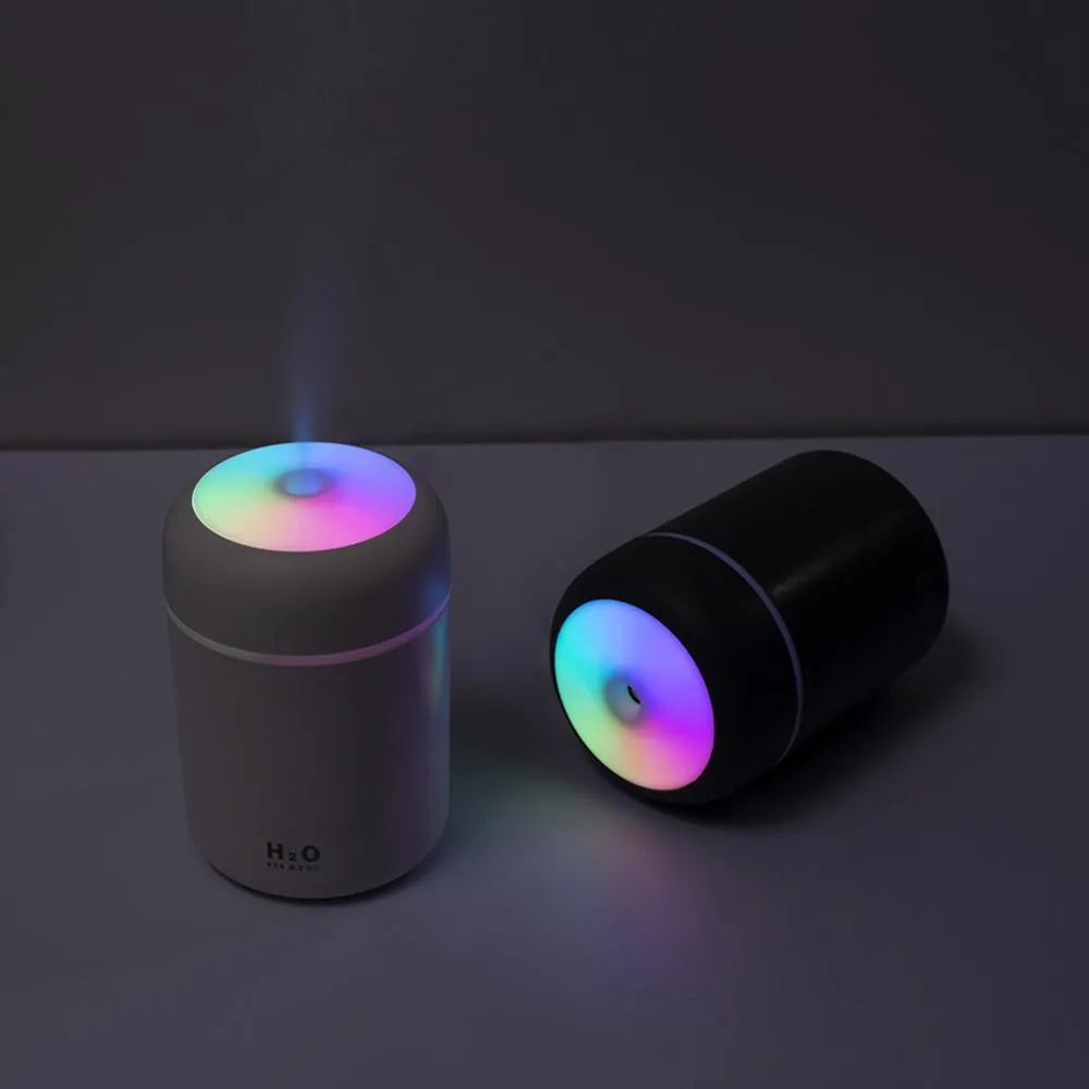 Pink USB desktop humidifier with LED lights and water tank on a wooden desk.