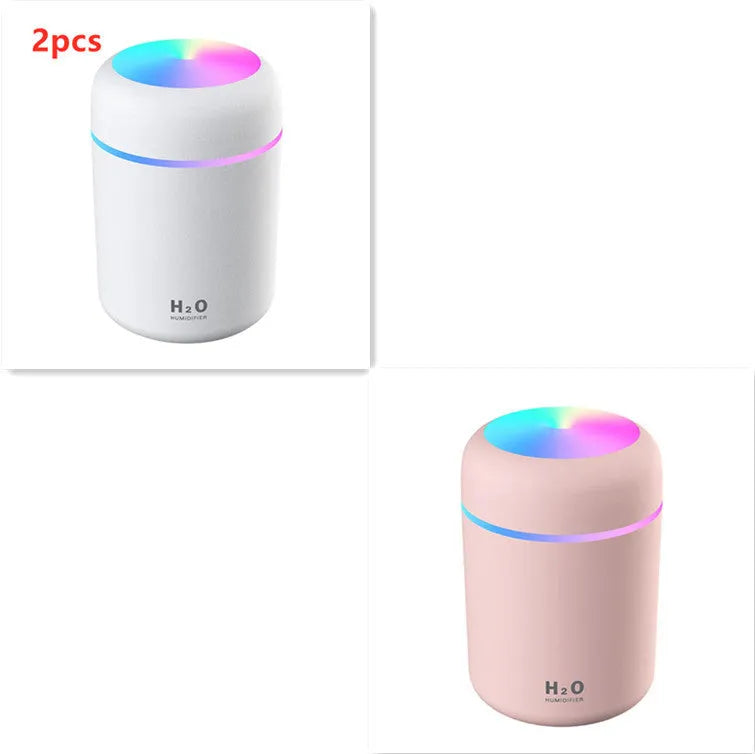 Pink USB desktop humidifier with LED lights and water tank on a wooden desk.