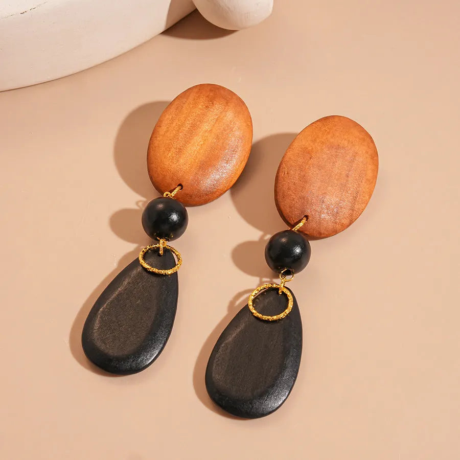 Handmade brown and black wooden ellipse earrings with silver needle fastenings on a white background.
