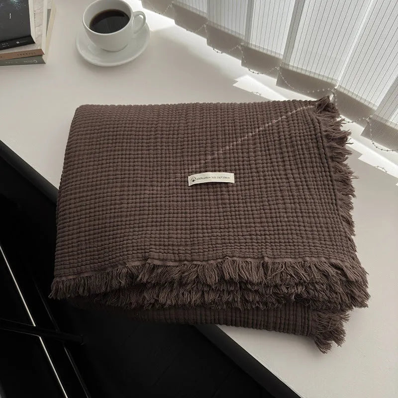 Cotton four-layer gauze blanket with tassel trim in various colours draped over a sofa.