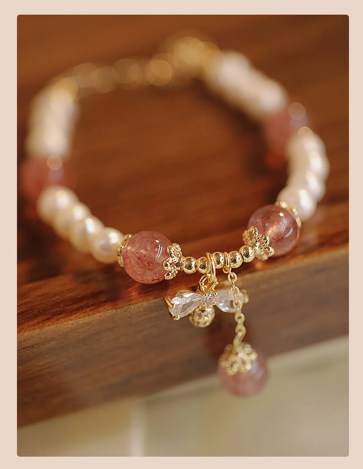 Women's strawberry quartz crystal bracelet with pearls and bow charm on wrist