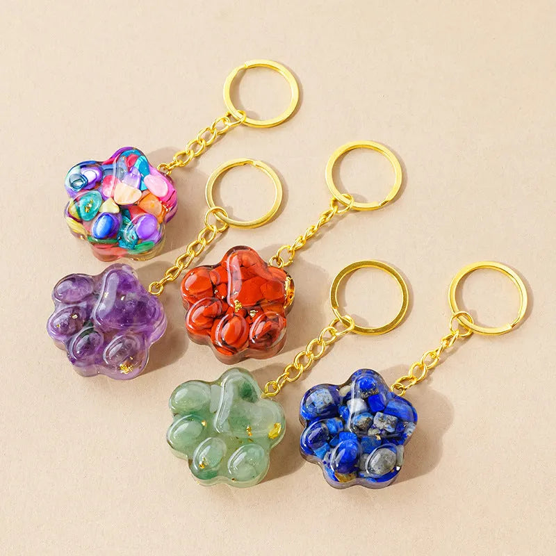 Small natural crystal cat's paw charm on a keyring, showing colour options including pink, red, blue, and purple gemstones.