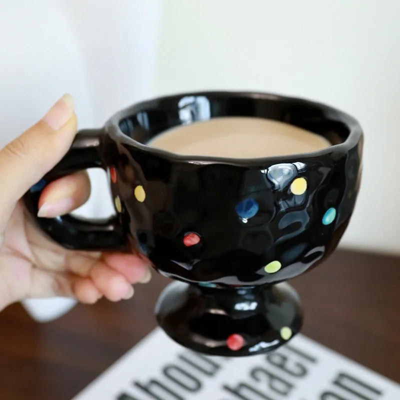 Hand-pinched irregularly shaped ceramic mug in a solid colour, shown on a table.