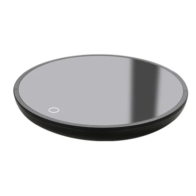 Black circular coffee mug warmer with a tempered glass surface on a desk.