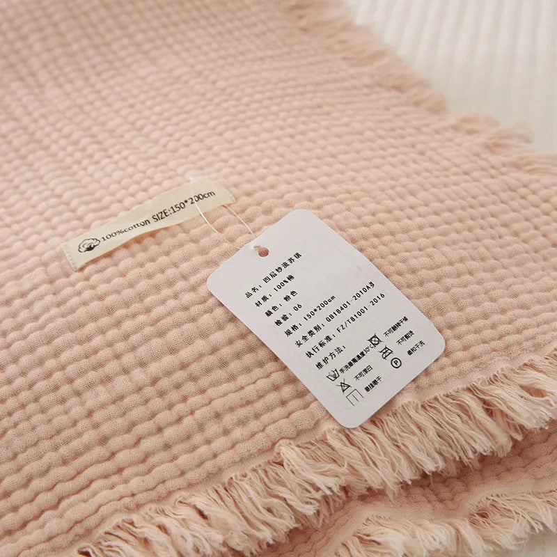 Cotton four-layer gauze blanket with tassel trim in various colours draped over a sofa.