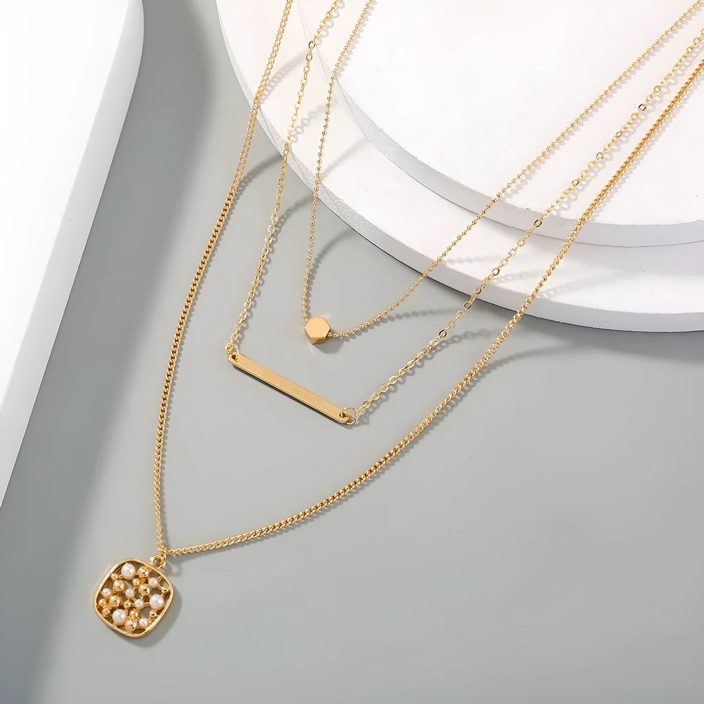 Gold multi-layer necklace with geometric pineapple pendant on a neutral background