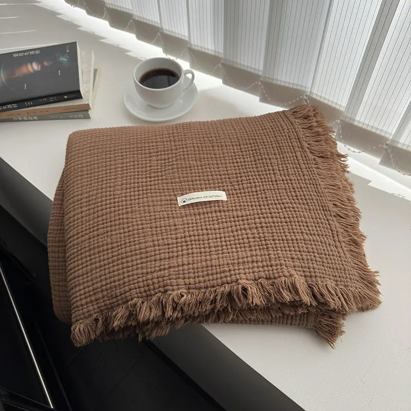 Cotton four-layer gauze blanket with tassel trim in various colours draped over a sofa.