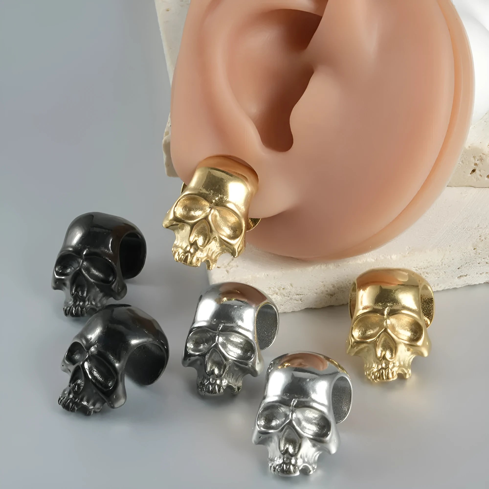 Stainless steel hollow skull Buddha earrings showing four colour finishes on geometry design