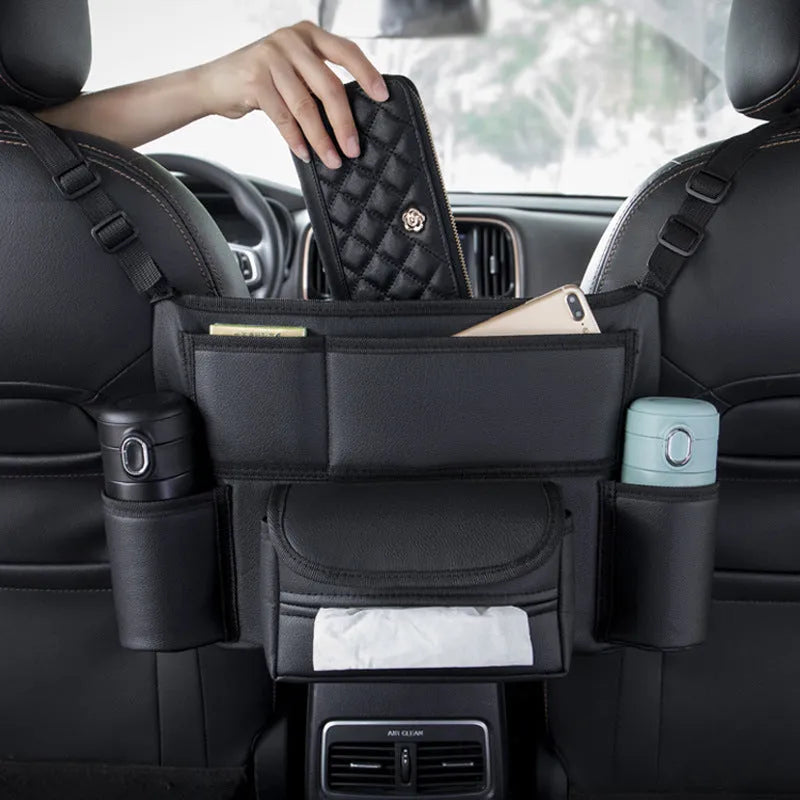 Black leather car interseat storage bag holding a tissue box, hanging between vehicle front seats.