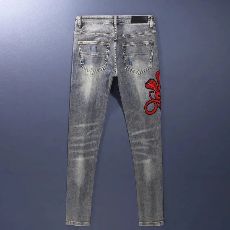 Men's old colour slim fit jeans with worn-out patches, holes, and embroidery on the legs.