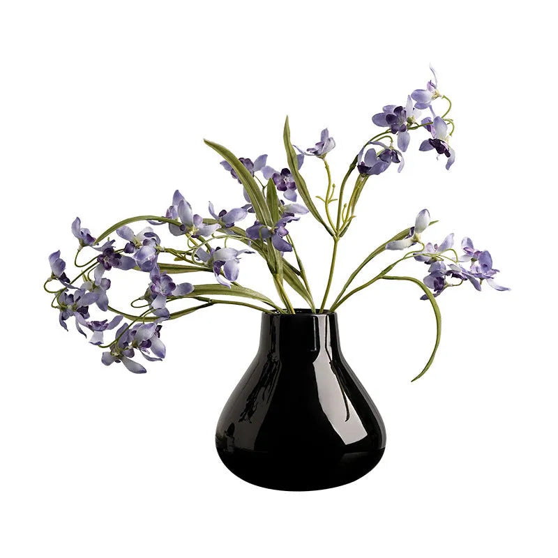 Black ceramic round belly vase with white artificial orchids on wooden table