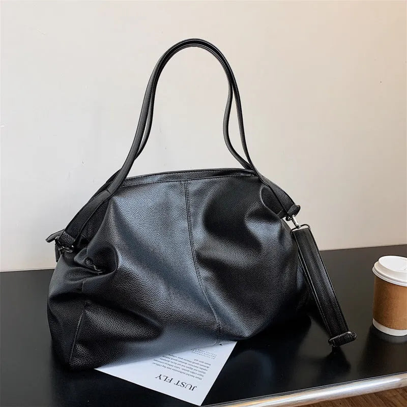 Large soft surface black messenger bag with soft handle and long shoulder strap on a table
