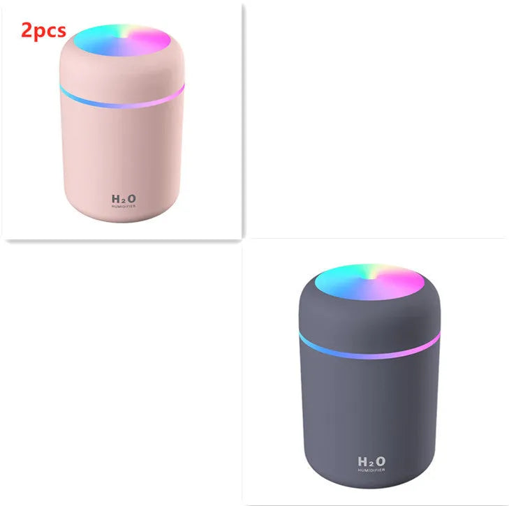 Pink USB desktop humidifier with LED lights and water tank on a wooden desk.