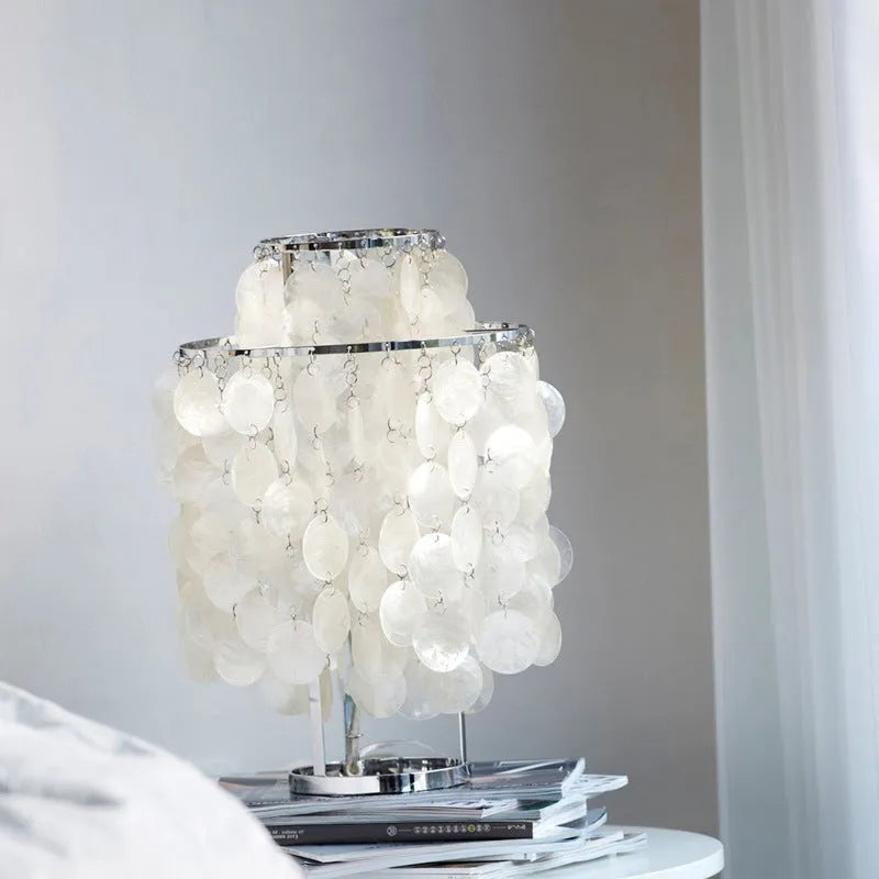 Creative modern shell-shaped table lamp in chrome or gold finish on a bedside table.