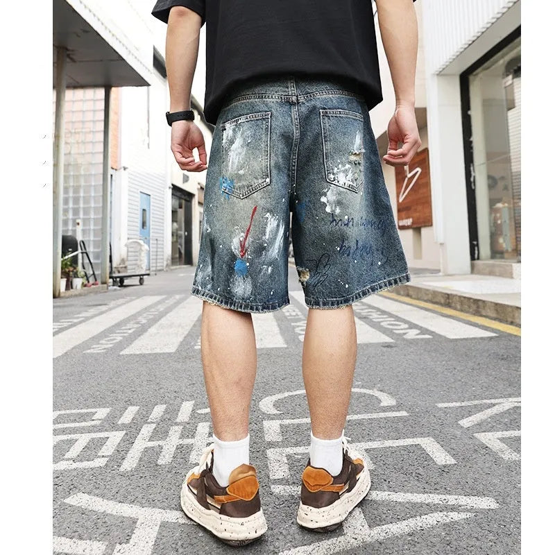 Blue men's denim shorts with ripped knees and graffiti detailing, showing straight leg cut and zipper fly.