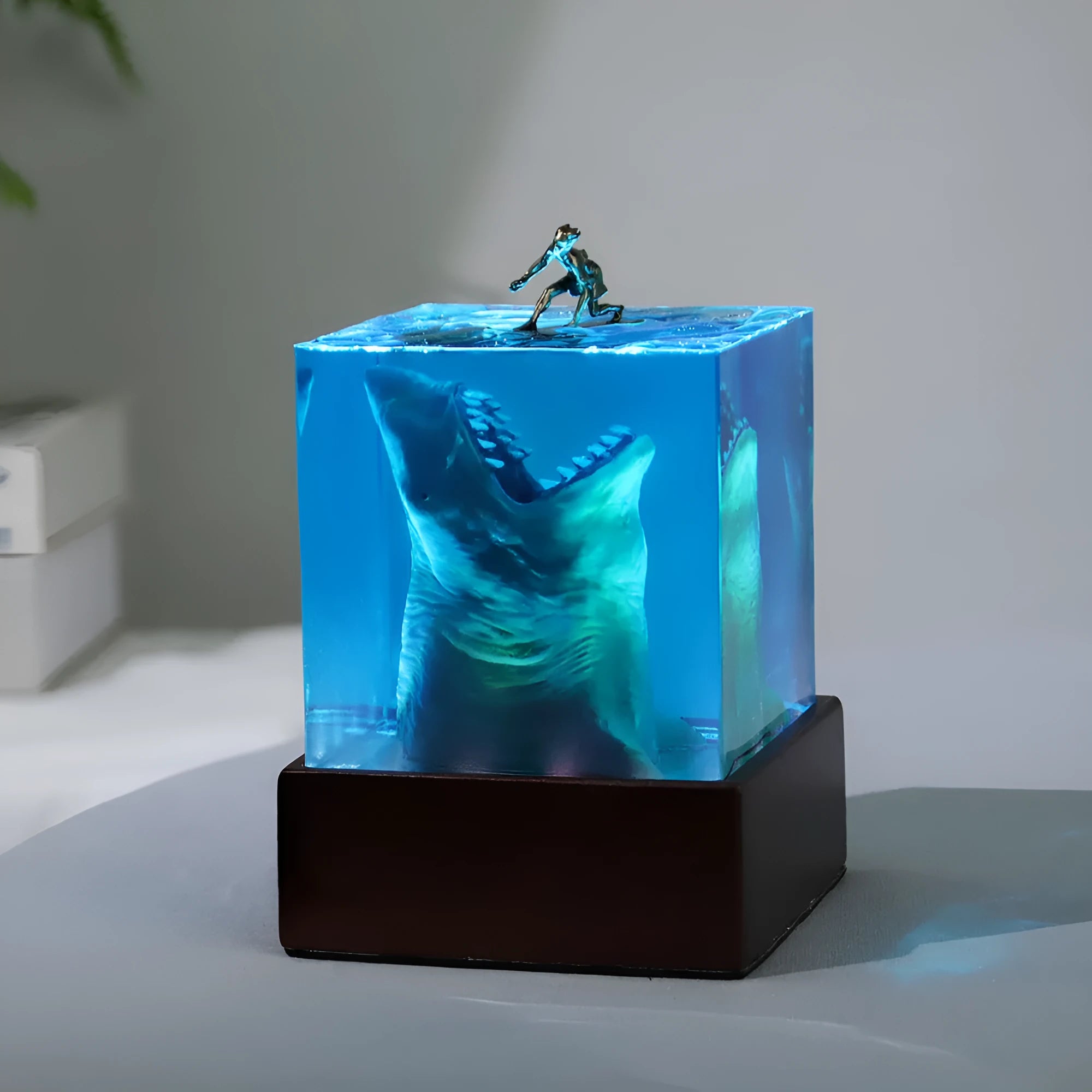 Close-up of a crystal resin shark surfer night light ornament on a dark surface.