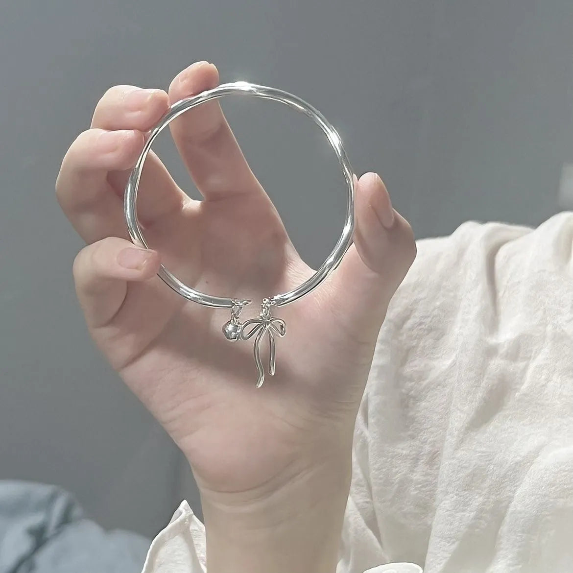 Silver tone adjustable bracelet with a bow charm on a white background.