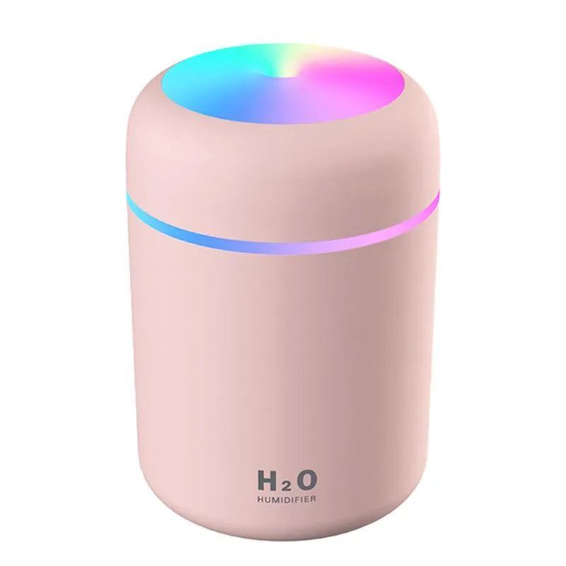 Pink USB desktop humidifier with LED lights and water tank on a wooden desk.