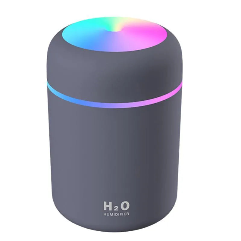 Pink USB desktop humidifier with LED lights and water tank on a wooden desk.