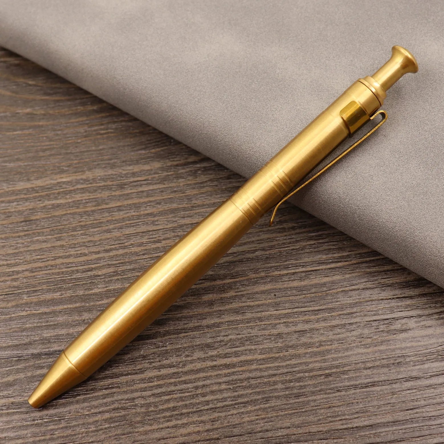 Close-up of a solid brass bolt action tactical pen with a press mechanism on a dark surface.