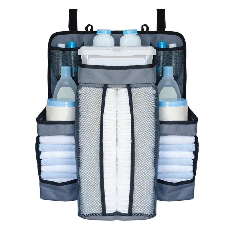 Gray baby diaper organizer hanging on a crib rail with compartments for nappies and wipes