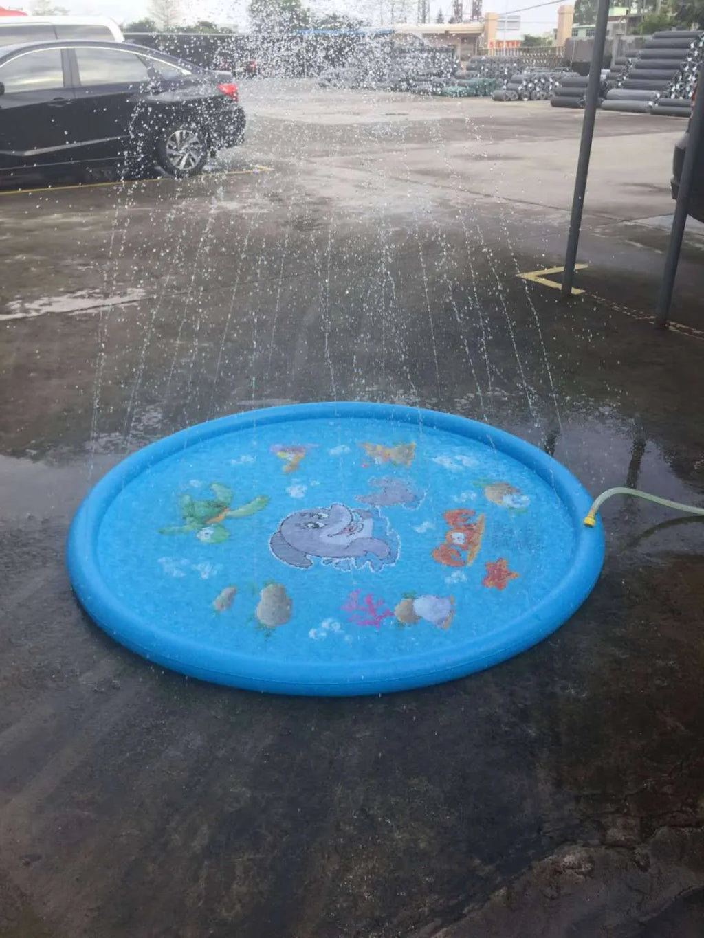 Blue PVC children's water spray play mat with marine animal designs, shown connected to a garden hose