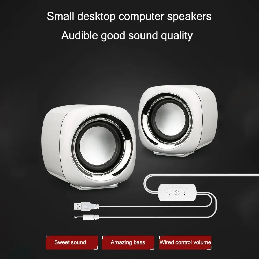 A pair of compact black wired desktop computer speakers with a volume scroll wheel, shown next to a 3.5mm audio plug.