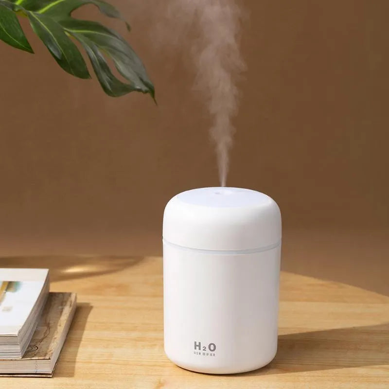 Pink USB desktop humidifier with LED lights and water tank on a wooden desk.