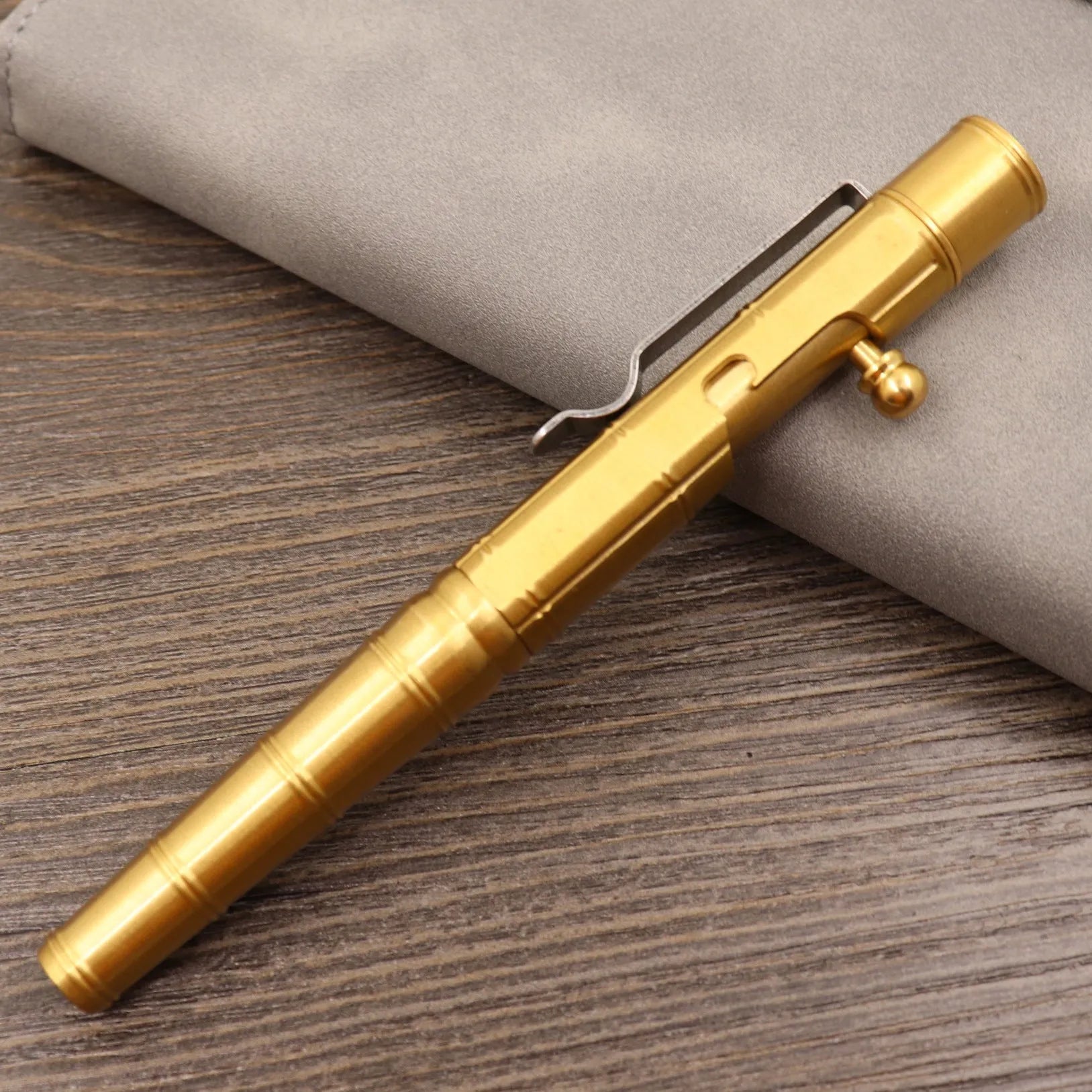 Close-up of a solid brass bolt action tactical pen with a press mechanism on a dark surface.