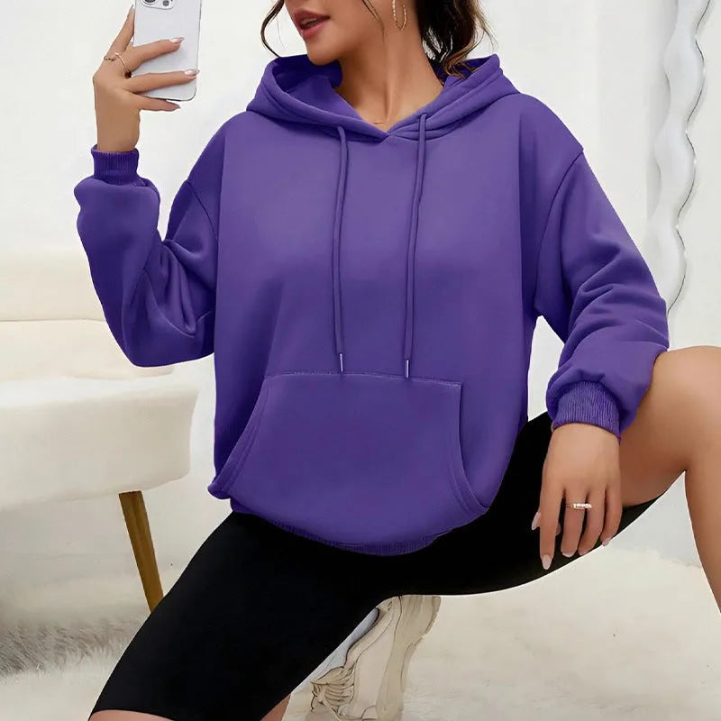 Woman wearing a loose-fitting black hooded sweatshirt with a front kangaroo pocket.