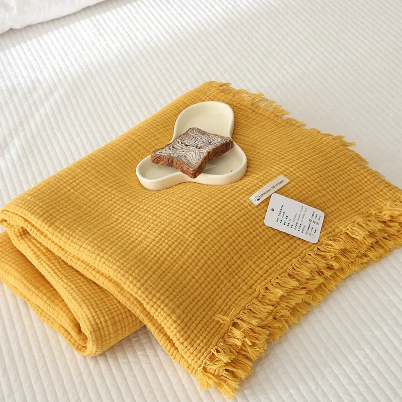 Cotton four-layer gauze blanket with tassel trim in various colours draped over a sofa.