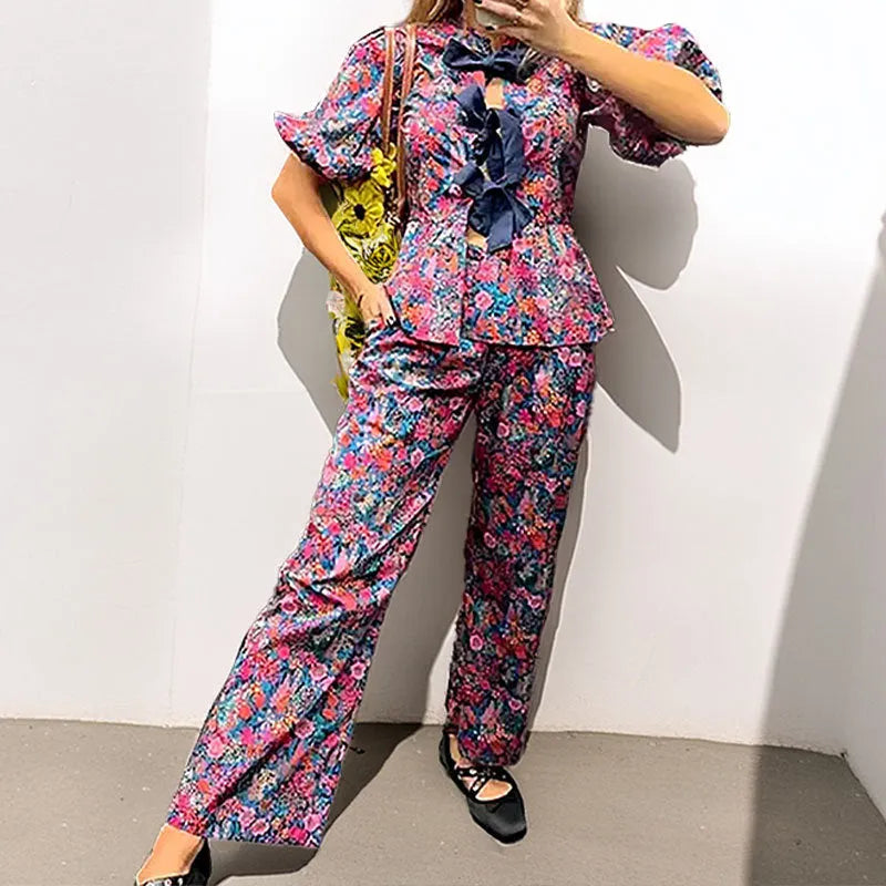 Women's floral print trousers suit with tie-neck puff sleeve top and matching trousers.